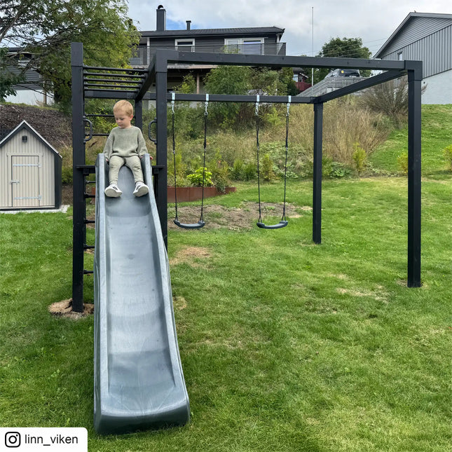 PLUS Daylife Schaukel 3 in einem Garten mit einem Bub auf der Rutsche