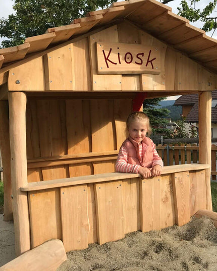 Ein Mädchen spielt im Spielhaus "Kiosk" in einem Garten