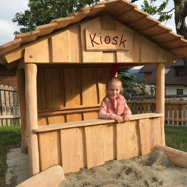 Ein Mädchen spielt im Spielhaus "Kiosk" in einem Garten
