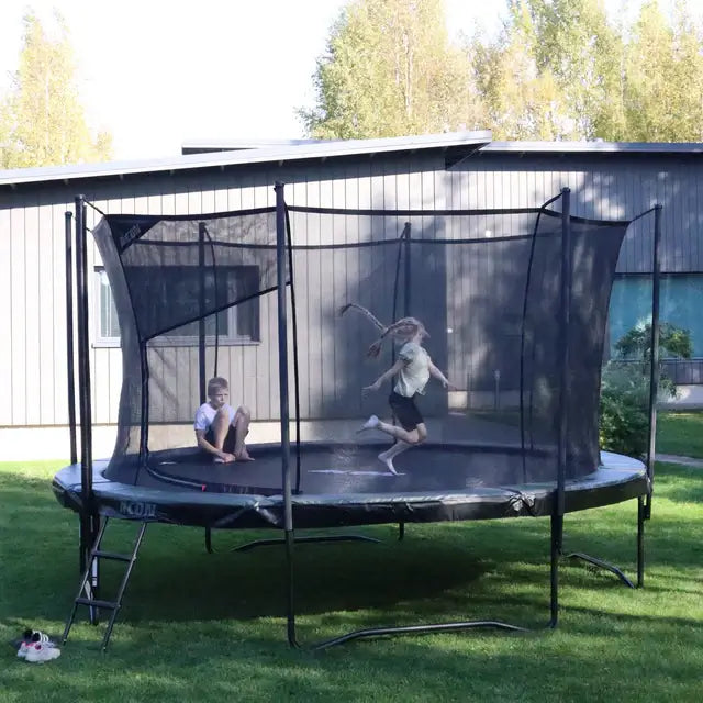 Zwei Kinder nutzen ein ACON AIR Gen 2.0 Rundtrampolin mit Sicherheitsnetz auf einer Rasenfläche im Garten.