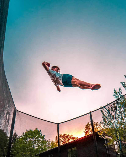 Person springt hoch auf einem ACON 16 HD Trampolin mit Sicherheitsnetz bei Sonnenuntergang.