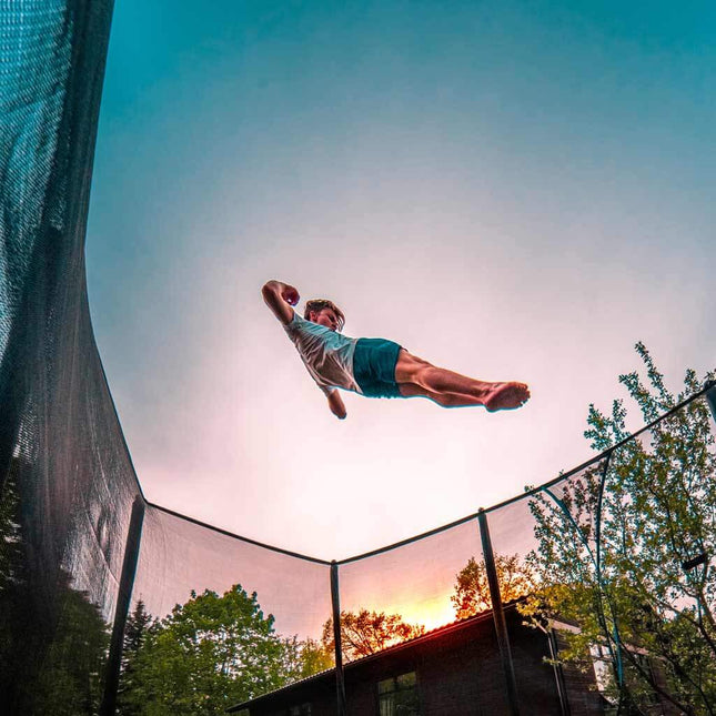 Person springt hoch auf einem ACON 16 HD Trampolin mit Sicherheitsnetz bei Sonnenuntergang.