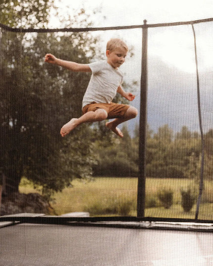 Kind springt auf einem ACON HD Trampolin mit umlaufendem Sicherheitsnetz im Garten.