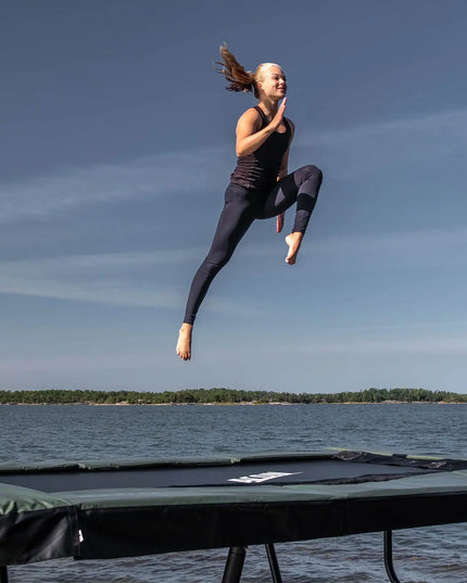 Turnerin führt einen hohen Sprung auf einem ACON 13 HD Trampolin am Wasser aus.