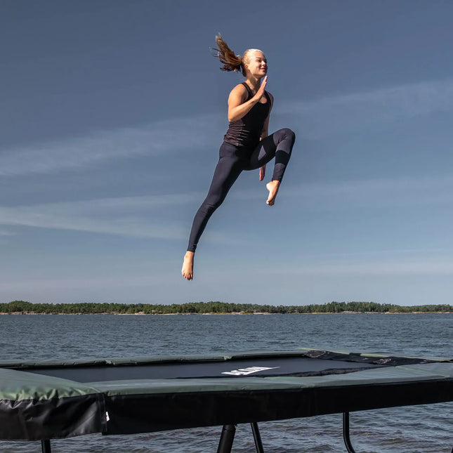 Turnerin führt einen hohen Sprung auf einem ACON 13 HD Trampolin am Wasser aus.