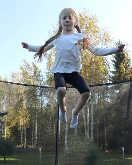Kind springt auf einem ACON AIR Gen 2.0 Rundtrampolin mit Sicherheitsnetz in einem Garten.