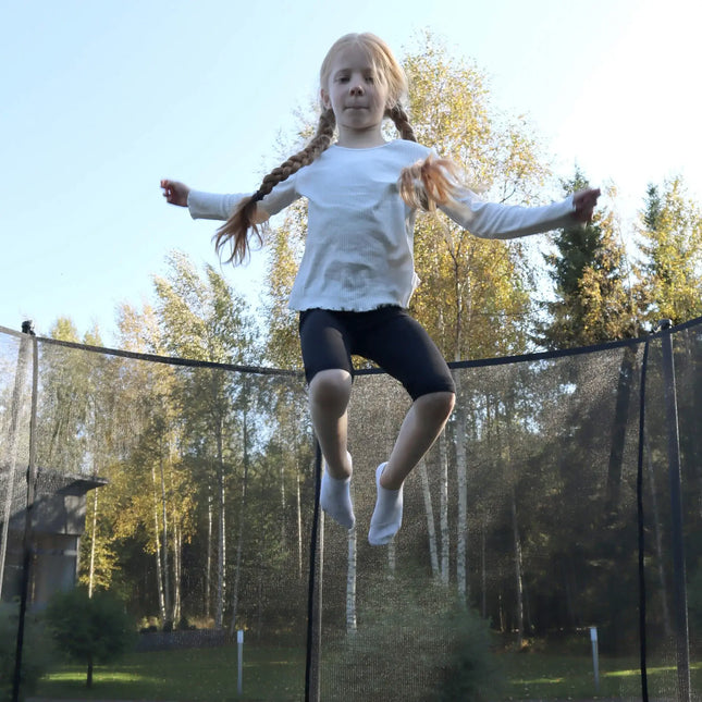 Kind springt auf einem ACON AIR Gen 2.0 Rundtrampolin mit Sicherheitsnetz in einem Garten.