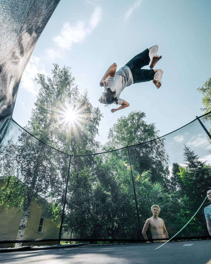Athlet führt einen Rückwärtssalto auf einem ACON HD PRO Trampolin mit Sicherheitsnetz im Garten aus.