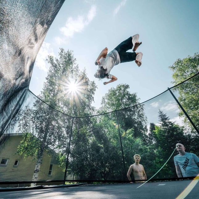 Athlet führt einen Rückwärtssalto auf einem ACON HD PRO Trampolin mit Sicherheitsnetz im Garten aus.